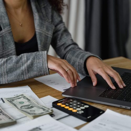 Woman using a laptop with cash and documents on desk in South Africa.