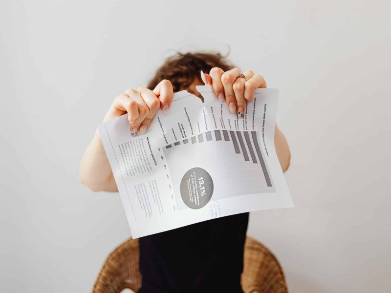 Person hiding face behind shredded document showcasing shredding services.